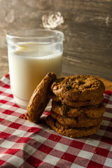 few homemade cookies with chocolate drops, stacked over each other, and a glass of milk. on red cloth table and wooden background. warm morning breakfast concept