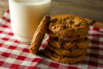 few homemade cookies with chocolate drops, stacked over each other, and a glass of milk. on red cloth table and wooden background. warm morning breakfast concept