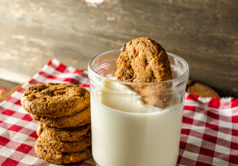 few homemade cookies with chocolate drops, stacked over each other, and a glass of milk. on red cloth table and wooden background. warm morning breakfast concept