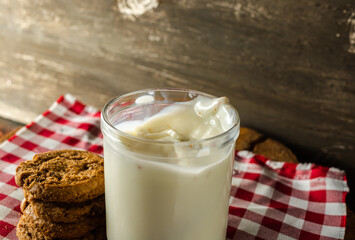 few homemade cookies with chocolate drops, stacked over each other, and a glass of milk. on red cloth table and wooden background. warm morning breakfast concept