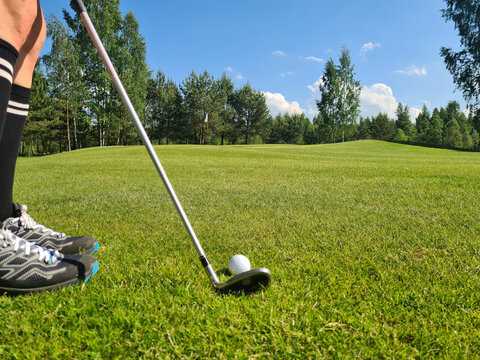 Closeup of white golf ball and club. Human feet on green grass