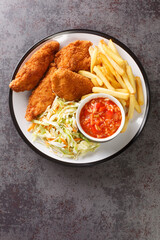 Breaded fried chicken with french fries, vegetable salad and spicy sauce close-up in a plate on the table. vertical top view from above