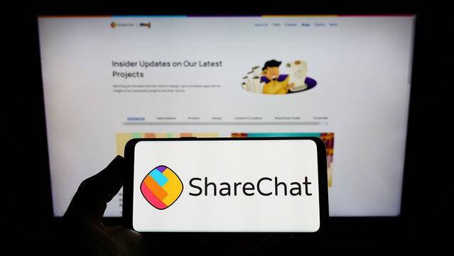 Stuttgart, Germany - 02-11-2022: Person holding mobile phone with logo of Indian company Mohalla Tech Pvt Ltd (ShareChat) on screen in front of web page. Focus on phone display.