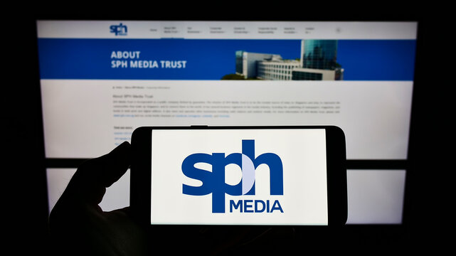 Stuttgart, Germany - 02-11-2022: Person holding mobile phone with logo of Singaporean company SPH Media Limited on screen in front of business web page. Focus on phone display.