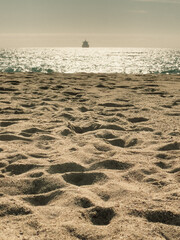 Footprints on sand and ship silhouette on calm sea at sunset in Reñaca beach, Chile. Peaceful dusk by Pacific Ocean