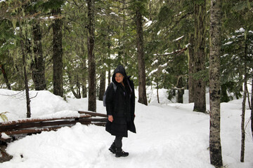 Latin adult woman with black jacket and gray backpack hiking in the snowy mountain very happy, free, full, positive, enjoys life and sports
