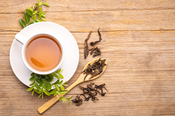 Obraz na płótnie Canvas White cup of hot tea and dry tea leaf on wooden table
