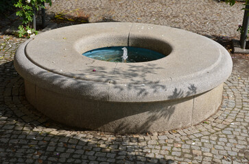 stone sandstone circular fountain in the park. built of sandstone filled with water. lined with a light threshing gravel road with a border of granite cubes, flowerbeds with orange flowers