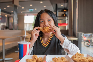 Close up portrait of a satisfied pretty  little asian girl eating fried chicken and french fries In the restaurant. Unhealthy food concept, close up