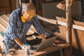 Fototapeta Senior builder wood worker using laptop computer at aiding design at construction work. obraz