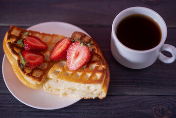 Belgian waffles with strawberries and coffee on a wooden, dark table.