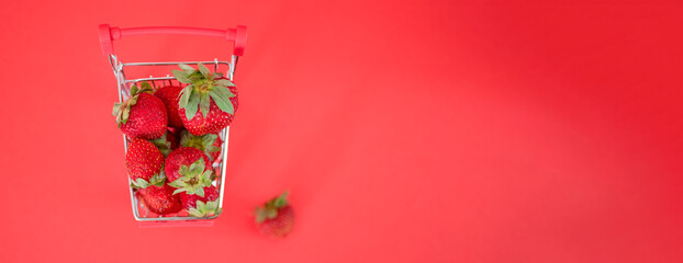 Small cart full of fresh ripe strawberries against a red background.