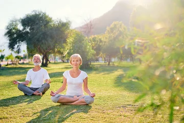 Foto op Canvas Yoga at park. Senior family couple  sitting in lotus pose on green grass. Concept of calm and meditation. © luengo_ua