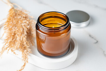 Natural wax candle on a white cocncrete tray and dry reeds decoration. Cozy lifestyle home interior decoration