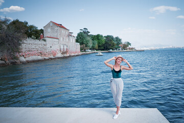 Tourism concept. Young traveling woman enjoying the view of Kastel Castle walking near the sea on Croatian coast. - obrazy, fototapety, plakaty