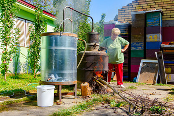 Woman is manually mixing fruit marc in distillation apparatus for making domestic alcohol liquor