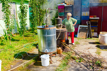 Woman is manually mixing fruit marc in distillation apparatus for making domestic alcohol liquor