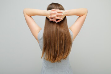 Woman in business dress standing back and holding hands on head, female portrait with long hair. Back view. Rear view.