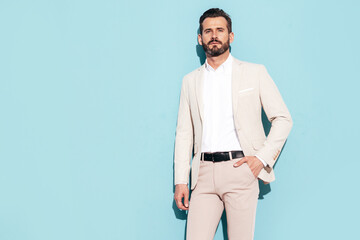 Portrait of handsome confident stylish hipster lambersexual model. Sexy modern man dressed in white elegant suit. Fashion male posing in studio near blue wall in sunglasses
