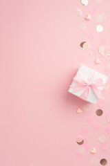 Gender party concept. Top view vertical photo of white giftbox with ribbon bow hearts and shiny confetti on isolated pastel pink background