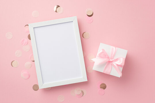 Baby girl concept. Top view photo of white giftbox with ribbon bow photo frame and shiny confetti on isolated pastel pink background with empty space
