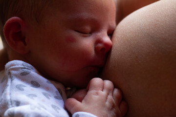 an adorable newborn baby sleeping on his mother's breast after breastfeeding