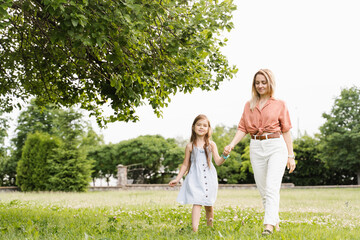 Naklejka na ściany i meble Mom and daughter walking and having fun together in the park. Happy family lifestyle. Love in family. Hapiness of mother and her child.