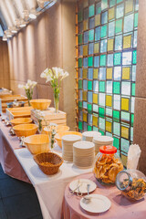 Flower arrangement for summer wedding, made of roses and green branches on a dinner table in the restaurant. , glass and plates in the restaurant outside on a windy day with film grain effect