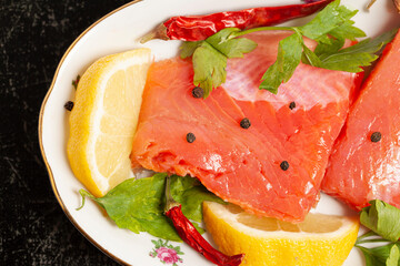 Pieces of lightly salted trout with herbs, spices and lemon on on a black background.
