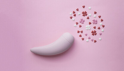 Pink vacuum stimulator toy for adults lies on a pink background, next to the decorative hearts mimic an orgasm. Conceptual photo. - 512930252