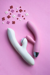 Two vibrators pink and white toy for adults lies on a pink background, next to decorative hearts mimic an orgasm. Conceptual photo. - 512930265