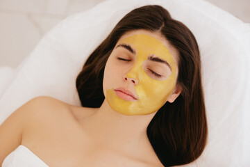 Close-up woman's face with golden mask. Facial Gold Mask. A woman lies on a cosmetology chair with...