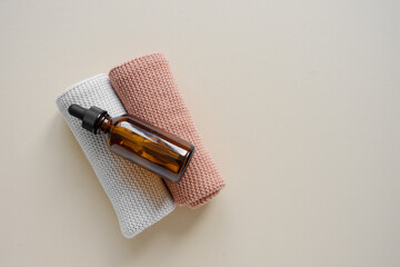 Eine braune Serum Flasche auf zwei zusammengerollte Handtücher. Beiger Hintergrund, Draufsicht.