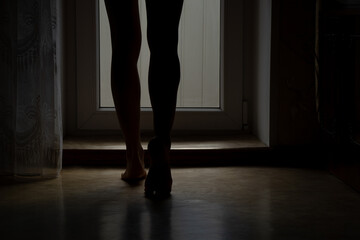 Women's feet on the floor at home near the window in the dark, feet on the floor