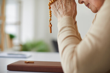 Senior woman praying. Humble religious mature lady sitting at table with Holy Bible, holding rosary...