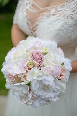 Young Caucasian bride wearing an elegant white dress while holding a large wedding bouquet of artificial roses and peonies, traditional accessory worn by the future wife as she walks down the aisle