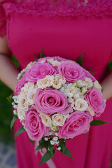 Close-up of a young woman wearing a hot pink dress while holding a classy round bouquet with matching large roses, lovely bridesmaid accompanying the bride on the wedding day or the marriage ceremony