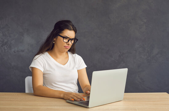 Unhappy Distressed Young Latin Woman In Glasses Sit At Table Work On Computer Frustrated By Bad Negative News. Mad Depressed Millennial Hispanic Female Confused Stressed With Laptop Problem.