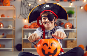Indoor shot of happy child dressed up in kid's pirate costume holding orange Halloween pumpkin...