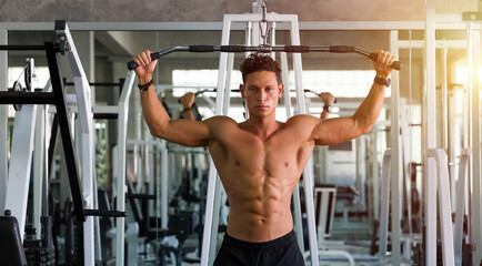 Fototapeta premium Muscular young man doing workout exercise with thrust of the upper block in the gym. Athletic man training hard in the sport gym.