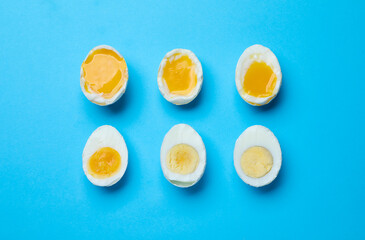 Different readiness stages of boiled chicken eggs on light blue background, flat lay