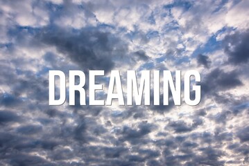 DREAMING - word on the background of the sky with clouds.