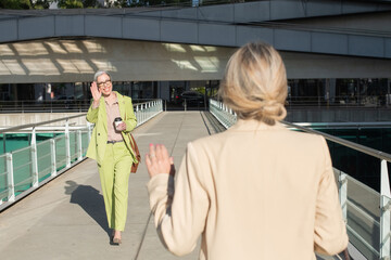 Businesswomen waving to each other in downtown area. Happy female friends in official suits meeting...