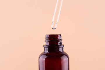 Oily drop dripping from pipette into cosmetic bottle close up, isolated on beige background.