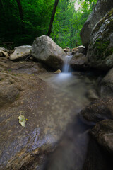 Naklejka na ściany i meble a small stream waterfall in the forest with rocks around