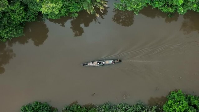 Aerial top down shot of boat cruising over amazon river in South America during cloudy day