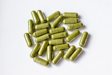 Closeup green herbal powder medicine capsule pill isolated on white background. Top view, selective...
