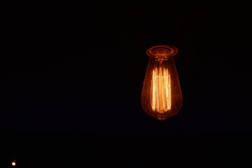 Classic lighting bulb in orange warm light over dark background.