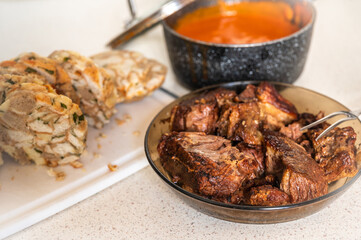 Sliced dumpling, baked piece of beef on brown plate, tomato sauce in pot.