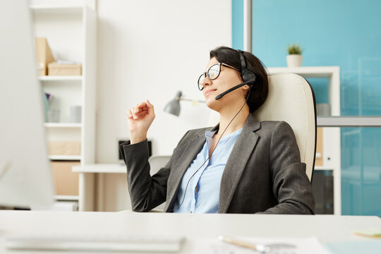 Content Relaxed Attractive Lady Boss In Formal Jacket Sitting At Table With Computer And Using Hands-free Device For Online Communication Over Internet, She Managing Team Remotely